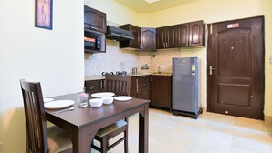 A compact kitchen with dark wooden cabinets, a microwave, a refrigerator, and a dining table with chairs.