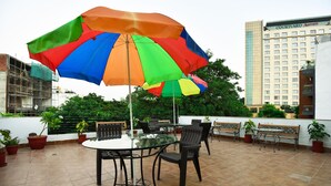 A terrace with a glass table and chairs, an umbrella, and potted plants.