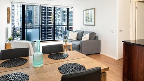 Uma sala de estar moderna com uma mesa de jantar de madeira, suportes para copos pretos e um sofá cinzento.