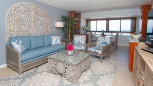 A living room with a blue sofa, patterned coffee table, and wicker chairs. - 1BR/1BA New Oceanside Condo (Charlotte Amalie)
