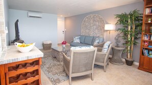 A living room with a sofa, chairs, a coffee table, a decorative wall piece, a potted plant, and a bookshelf. - 1BR/1BA New Oceanside Condo (Charlotte Amalie)