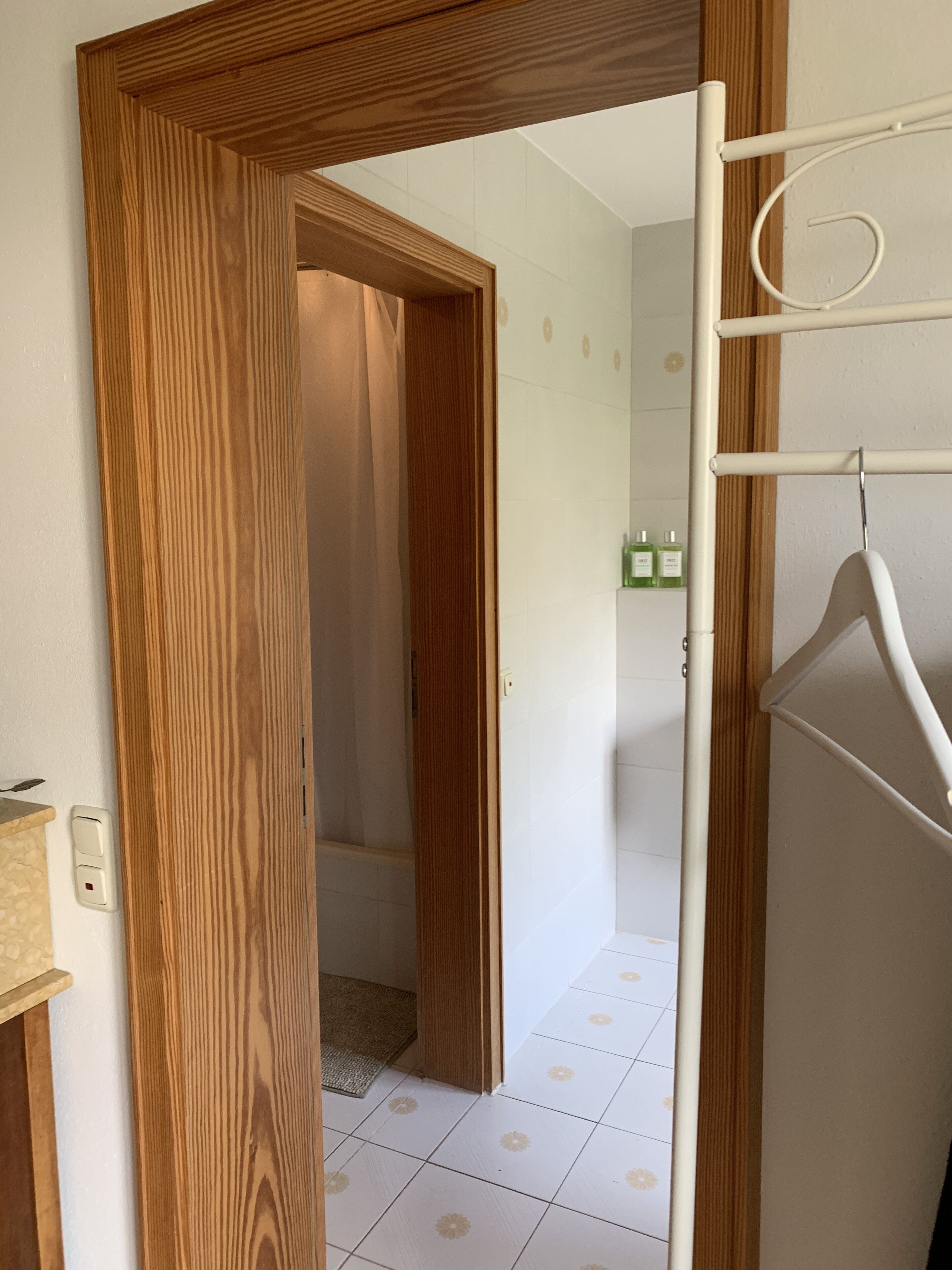 Eine Holztür führt zu einem Badezimmer mit weißen Fliesen und einer Duschkabine.