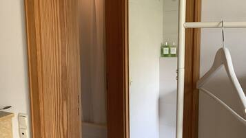 Eine Holztür führt zu einem Badezimmer mit weißen Fliesen und einer Duschkabine.