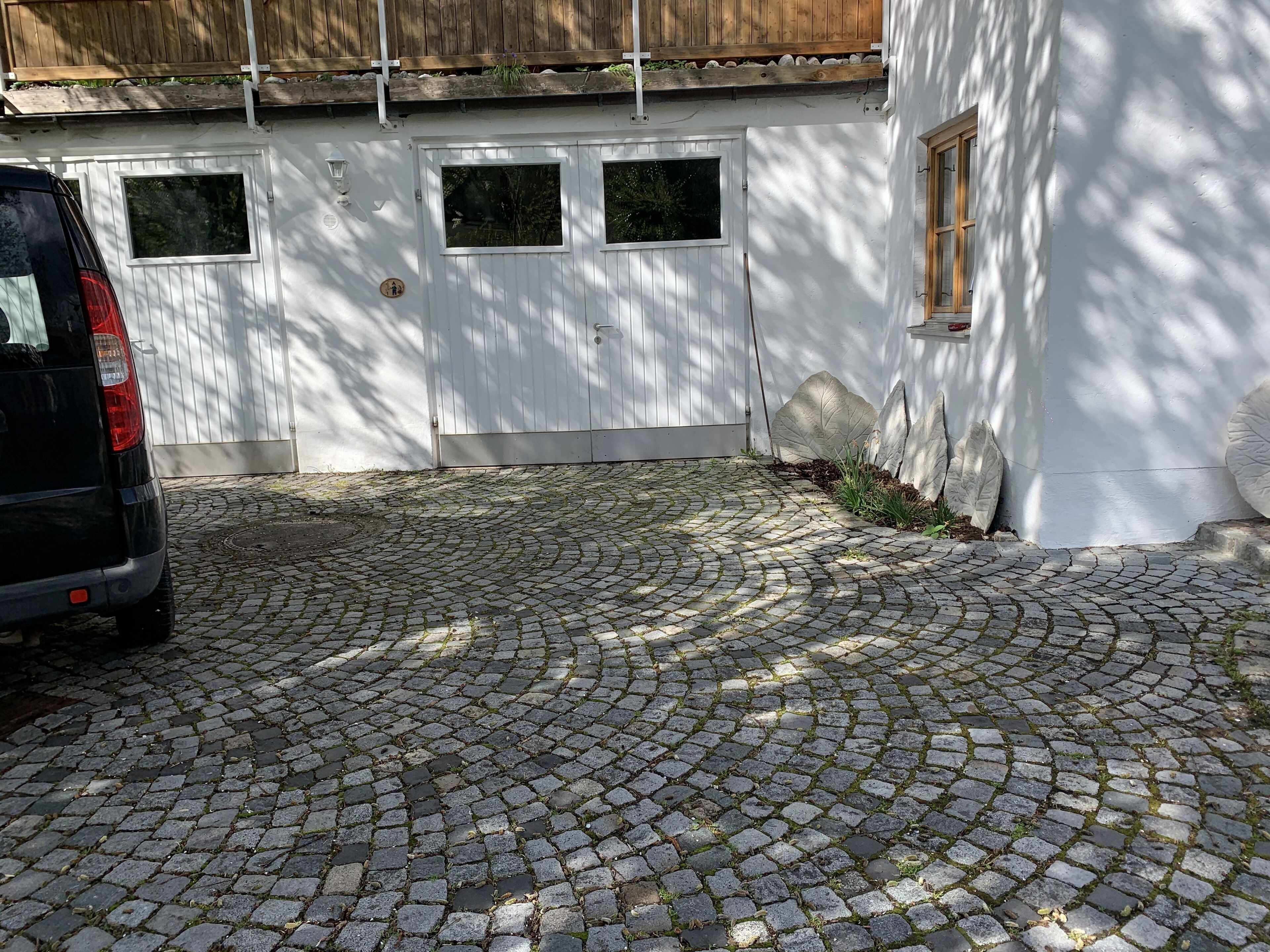 Ein gepflasterter Weg führt zu einem weißen Gebäude mit einer Holztür und Fenstern.