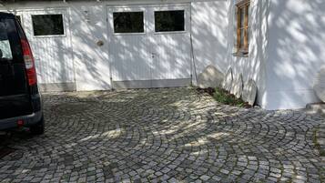 Ein gepflasterter Weg führt zu einem weißen Gebäude mit einer Holztür und Fenstern.