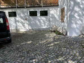 Um caminho de paralelepípedos leva a um edifício branco com porta e janelas de madeira.