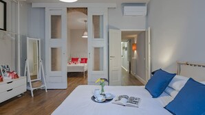 A bedroom with a bed, bedside table, and a mirror. There is a hallway leading to another room with a bed. - Guelfa Apartment  (Firenze)