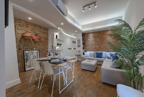 A modern living room with a dining area, featuring a stone wall, a sofa set, and a potted plant.