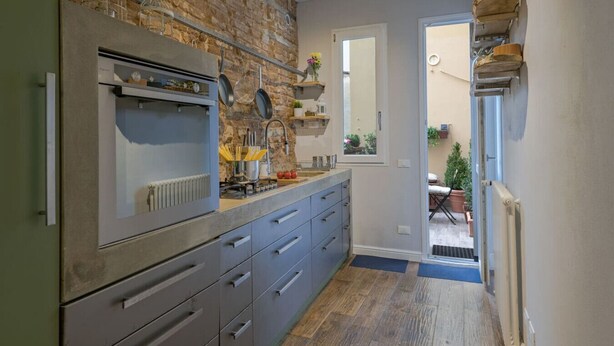 A kitchen with a brick wall, a built-in oven, and a sink. There are cabinets and a countertop with various kitchen items. - Guelfa Apartment  (Firenze)