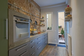A kitchen with a brick wall, a built-in oven, and a sink. There are cabinets and a countertop with various kitchen items.