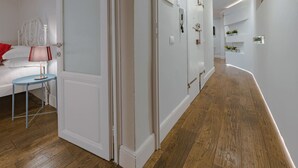 A modern hallway with wooden flooring, white walls, and a bed with a red pillow. - Guelfa Apartment  (Firenze)