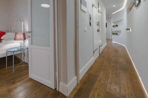 A modern hallway with wooden flooring, white walls, and a bed with a red pillow.