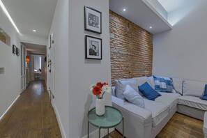 A modern living room with a white sofa, a glass coffee table, and a brick accent wall. There are framed pictures on the wall and a vase with flowers on the table. - Guelfa Apartment (Firenze)