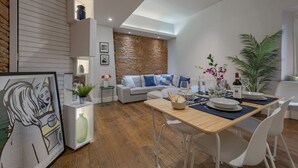 A modern living room with a dining area, featuring a stone accent wall, a sofa with blue cushions, and a dining table set for four. - Guelfa Apartment  (Firenze)