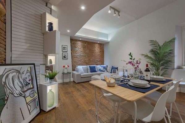 Uma sala de estar moderna com área de jantar, destacando uma parede de pedra, um sofá com almofadas azuis e uma mesa de jantar posta para quatro pessoas.