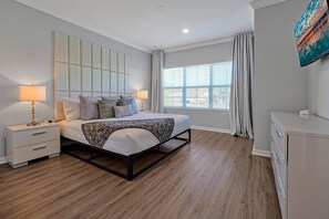 A modern bedroom with a bed, bedside tables, a dresser, and a large window with curtains. - Cozy 2bdrs w/ private jacuzzi & lake view (Kissimmee)