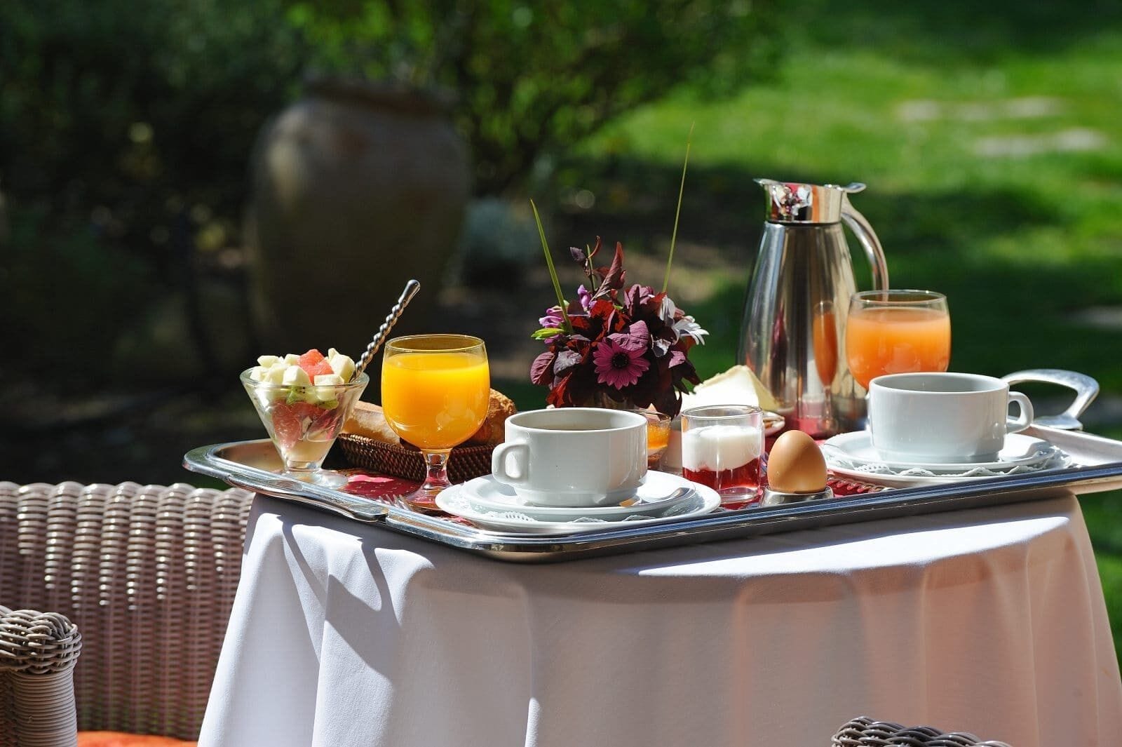Ein Frühstücksbrett mit verschiedenen Speisen und Getränken, darunter ein Glas Orangensaft, eine Tasse Kaffee und eine Karaffe Orangensaft, draußen auf einem Tisch.