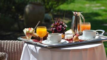 Ein Frühstücksbrett mit verschiedenen Speisen und Getränken, darunter ein Glas Orangensaft, eine Tasse Kaffee und eine Karaffe Orangensaft, draußen auf einem Tisch.