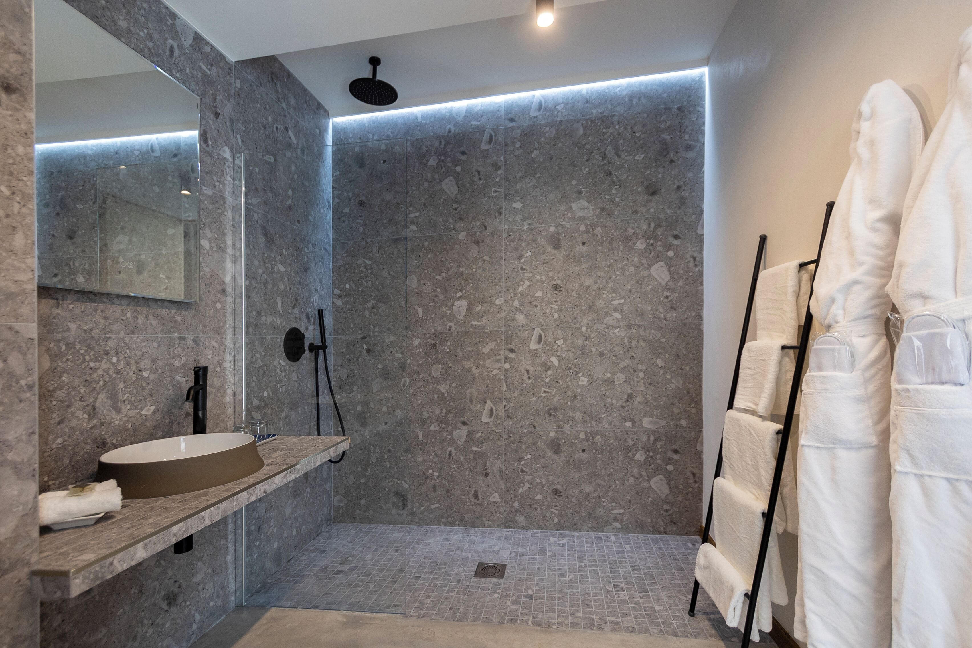 Un baño moderno con un espejo grande, un lavabo redondo, una ducha con grifo negro y toallas colgadas en un perchero.