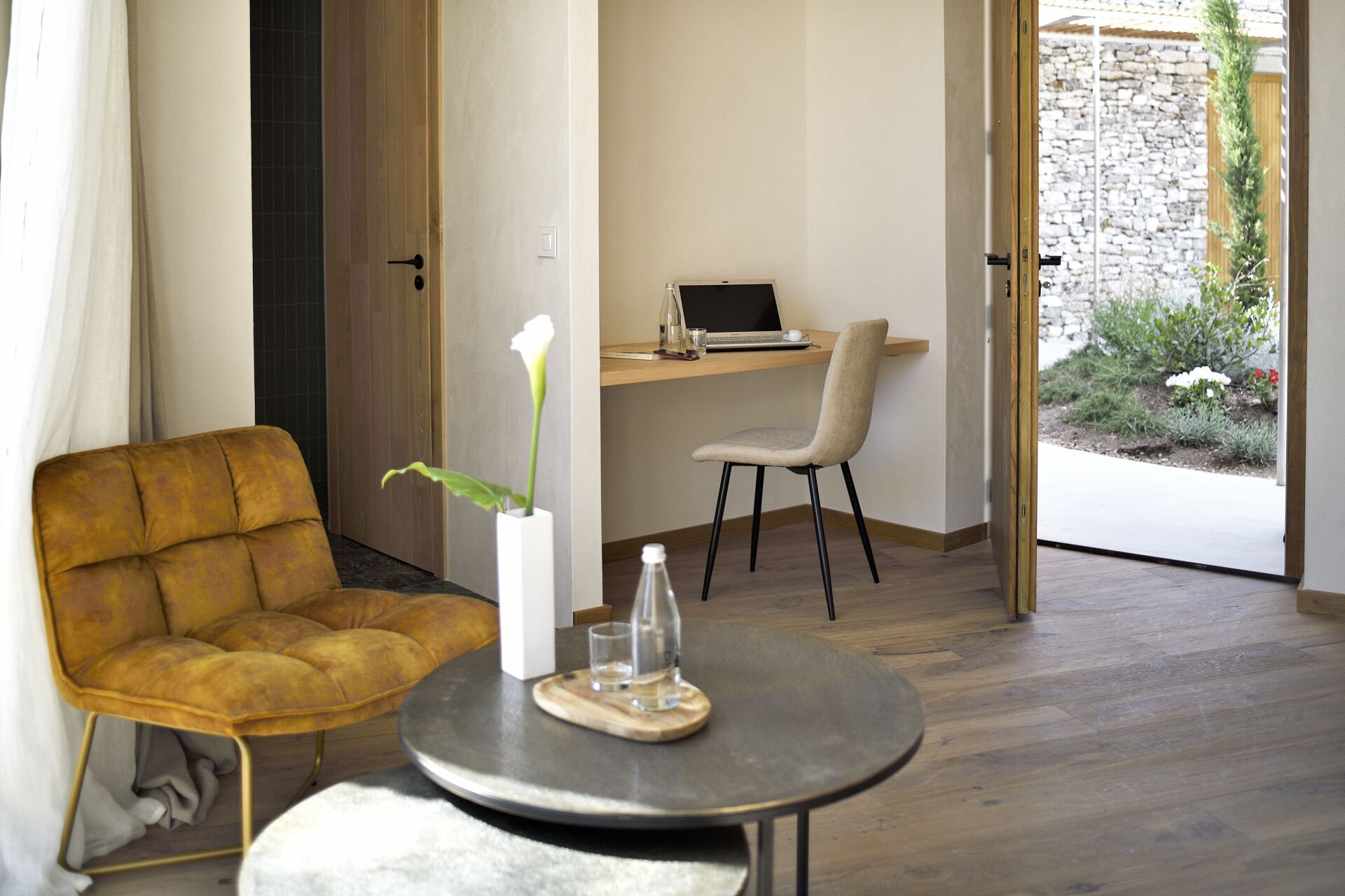 Una habitación moderna con piso de madera, un sofá, una mesa redonda con un vaso y una laptop sobre un escritorio.