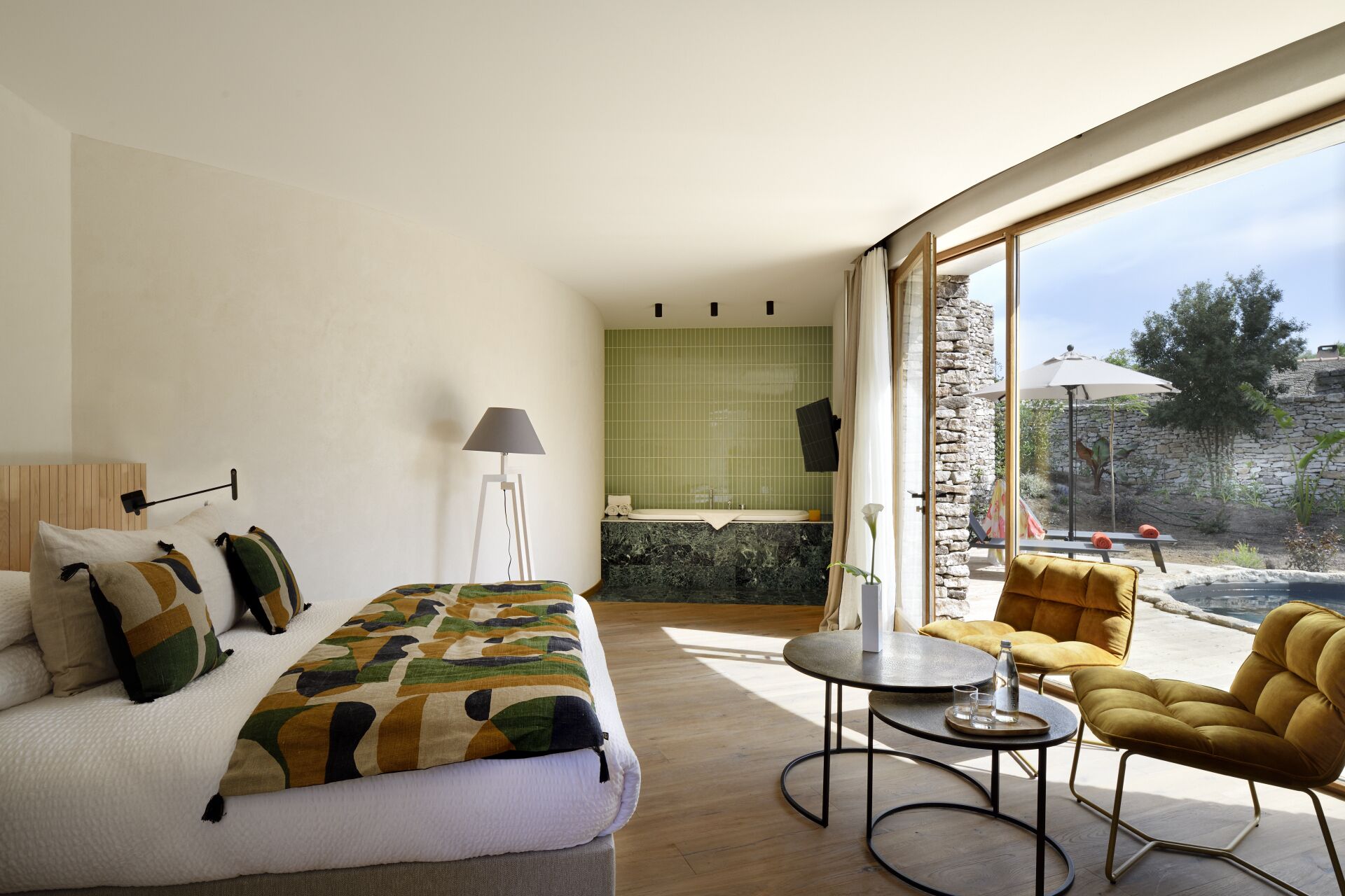 A bedroom with a bed, bedside lamp, and a view of a bathroom with a bathtub.