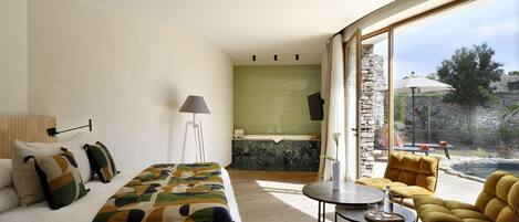 A bedroom with a bed, bedside lamp, and a view of a bathroom with a bathtub.