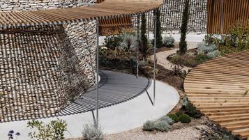 Un espacio exterior moderno con un muro de piedra, pérgolas de madera y un sendero curvo.