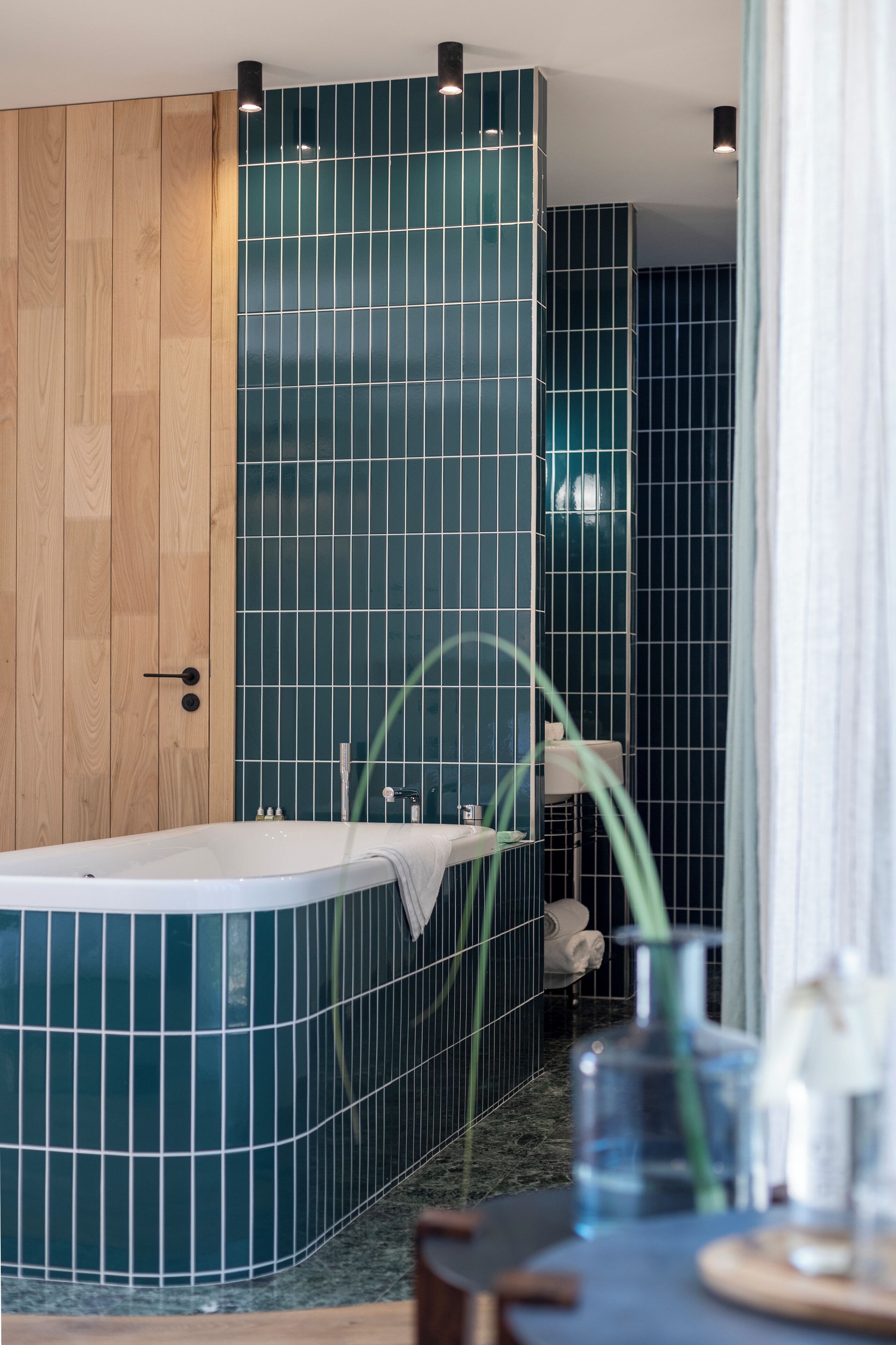 A modern bathroom with a freestanding bathtub, wooden paneling, and dark blue tiled walls.
