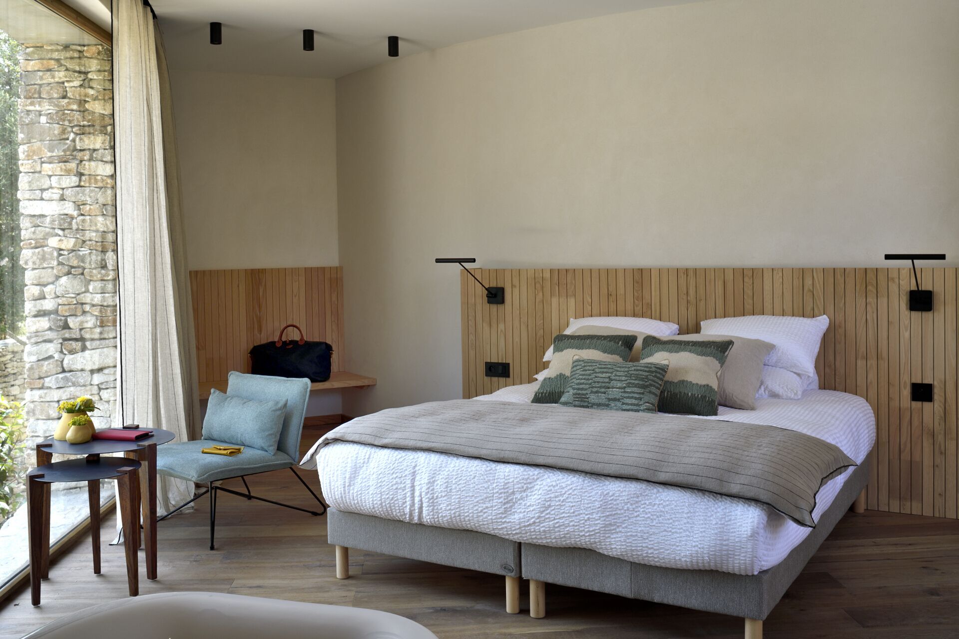 Ein Schlafzimmer mit einem Bett, einem Sessel, einem kleinen Tisch und einer Steinwand.
