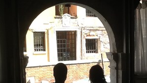 A couple sitting at a table in a dimly lit room with an arched doorway leading to a courtyard with brick buildings.