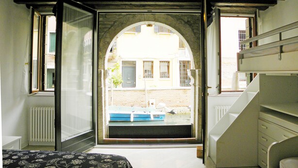 A room with a bed, a window, and a view of a building outside.