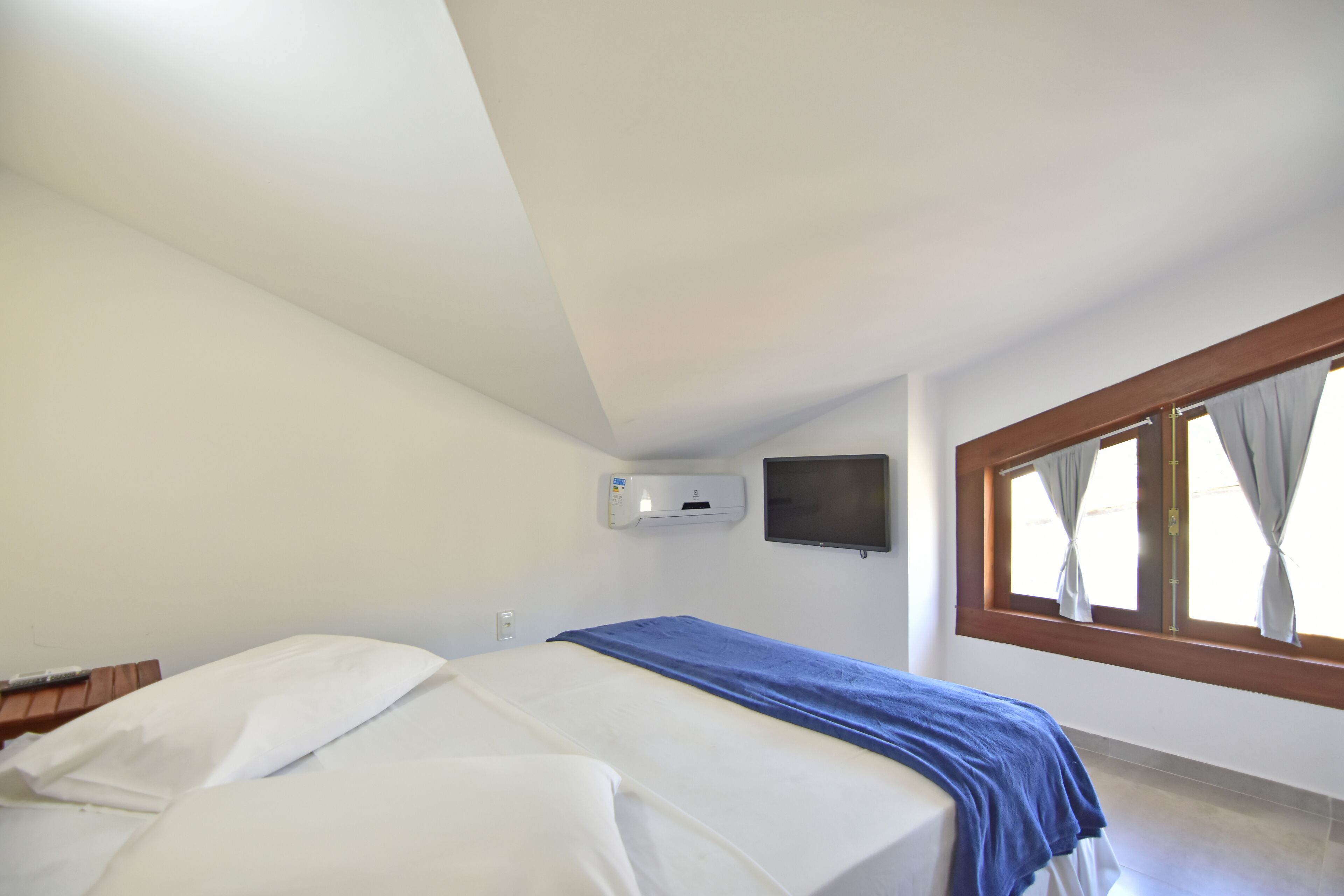 A bedroom with two beds, a flat-screen TV mounted on the wall, and a window with curtains.