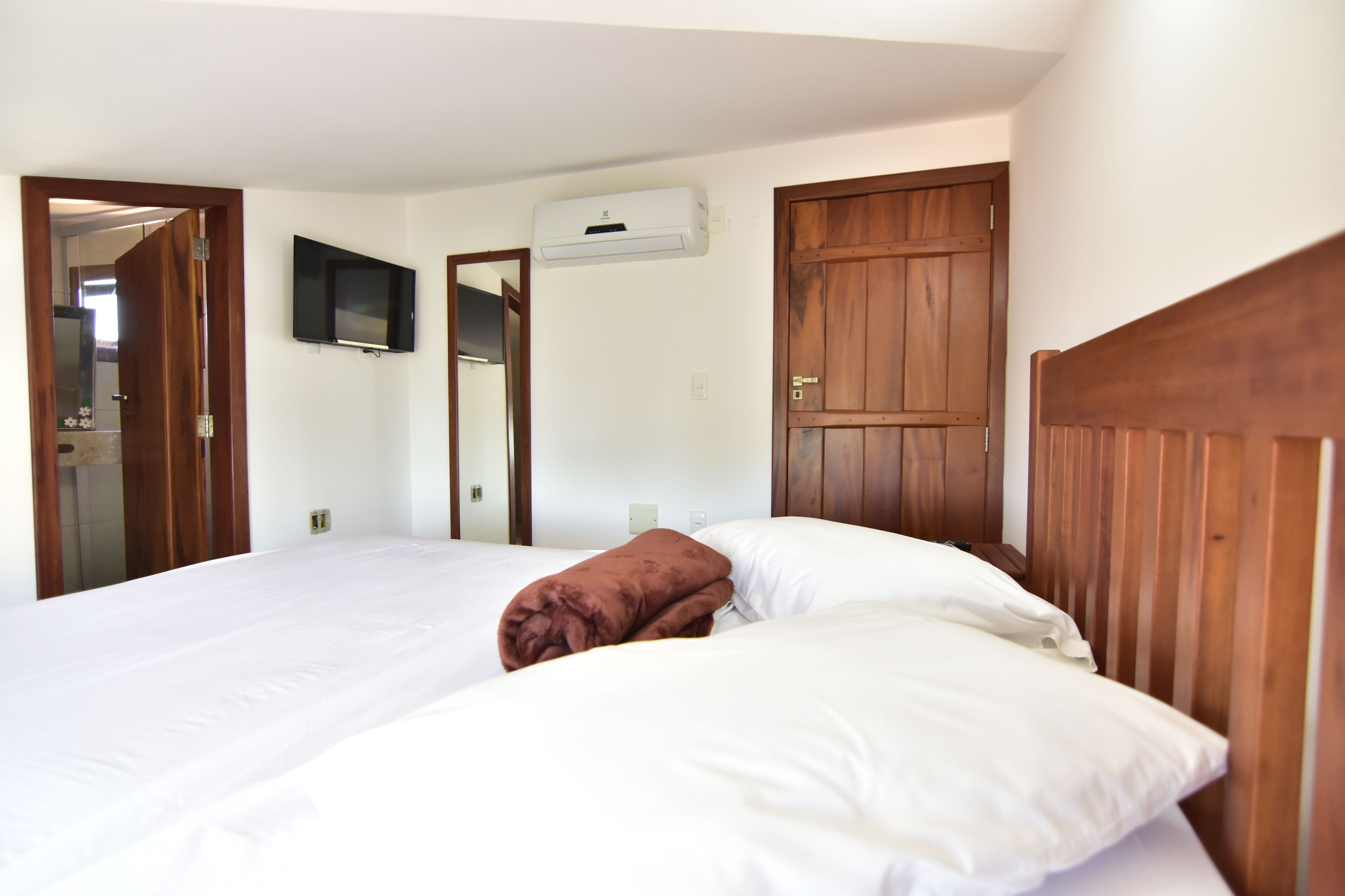 A hotel room with a bed, a TV mounted on the wall, and an air conditioning unit.