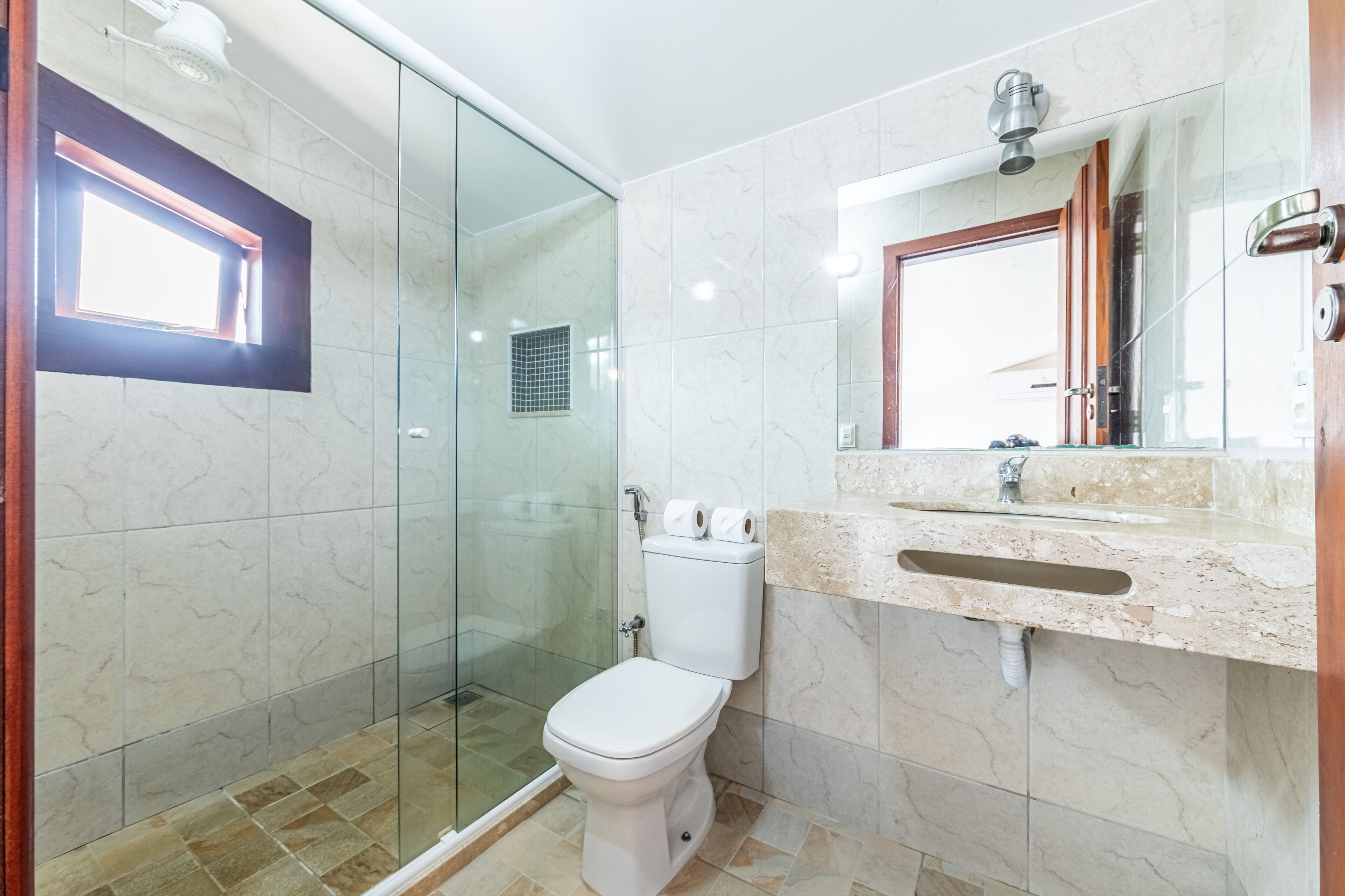 Un baño moderno con ducha de vidrio, inodoro y lavabo con encimera de mármol.
