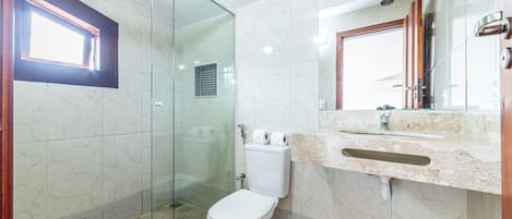 Un baño moderno con ducha de vidrio, inodoro y lavabo con encimera de mármol.