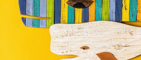 Un objeto de madera con una silueta recortada y una mancha marrón, sobre un fondo amarillo con listones de madera verticales de colores.