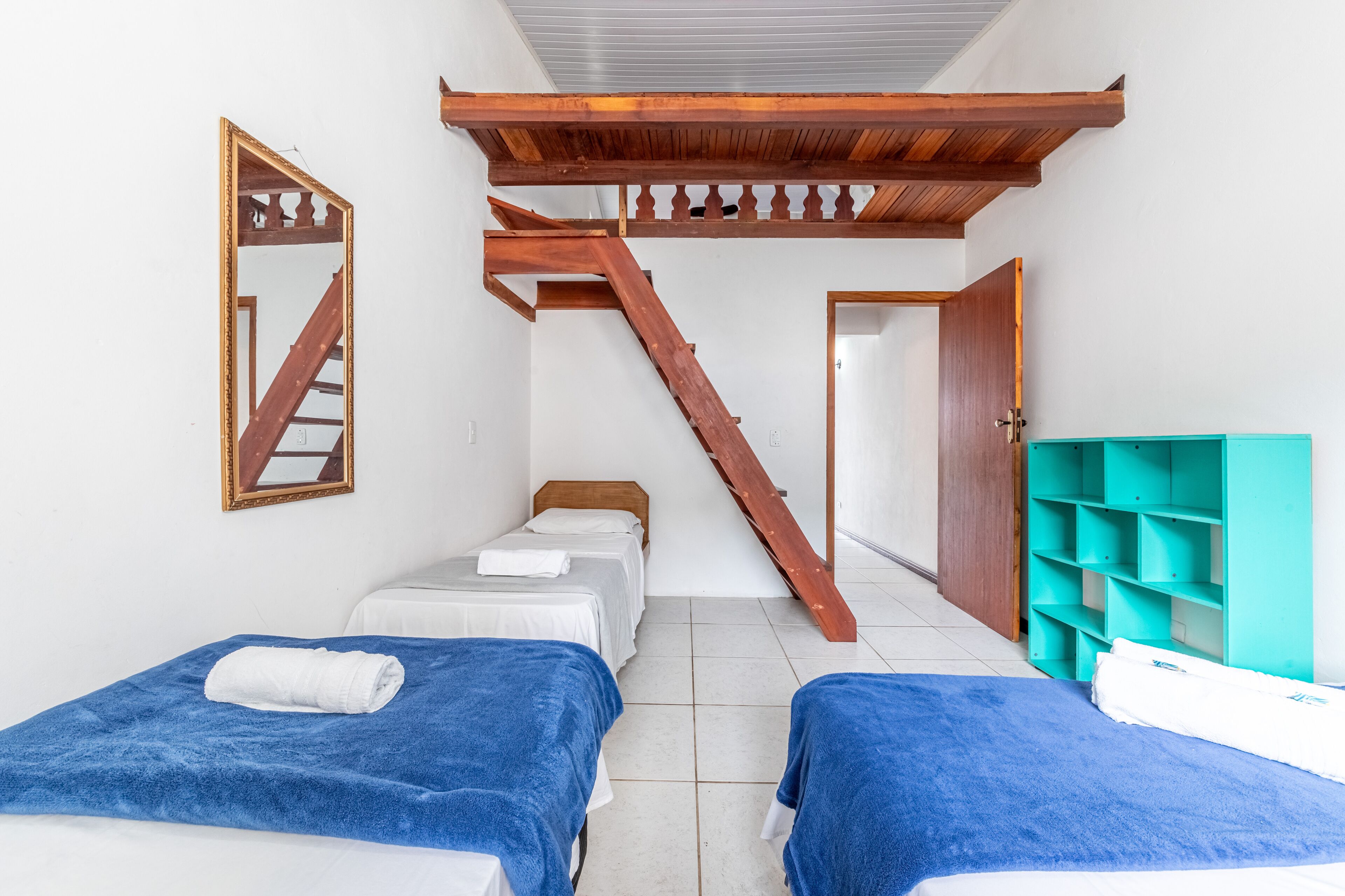 A room with two beds, a wooden staircase, a mirror, and a teal storage unit.