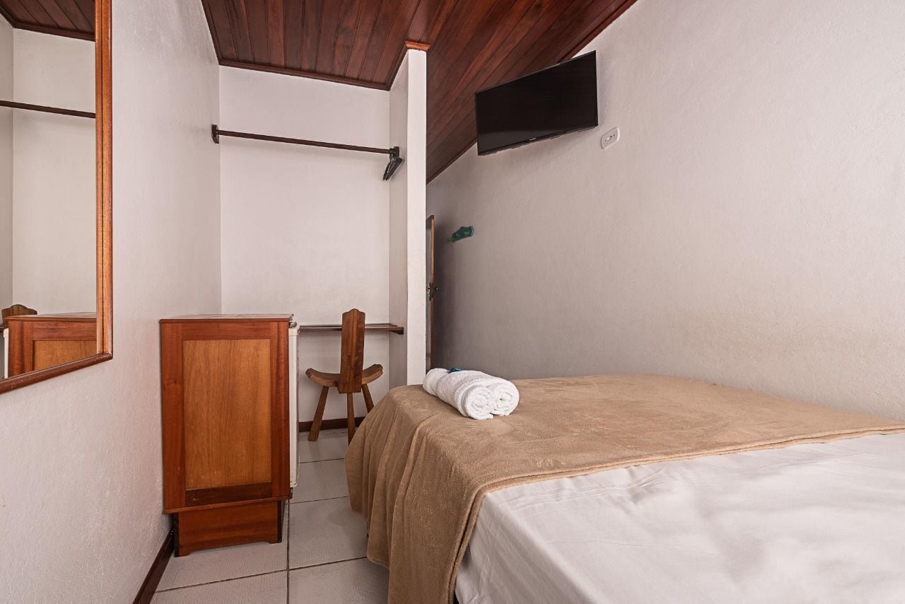 Une chambre à coucher comprenant un lit, une armoire en bois, une chaise, un miroir et un téléviseur fixé au mur.