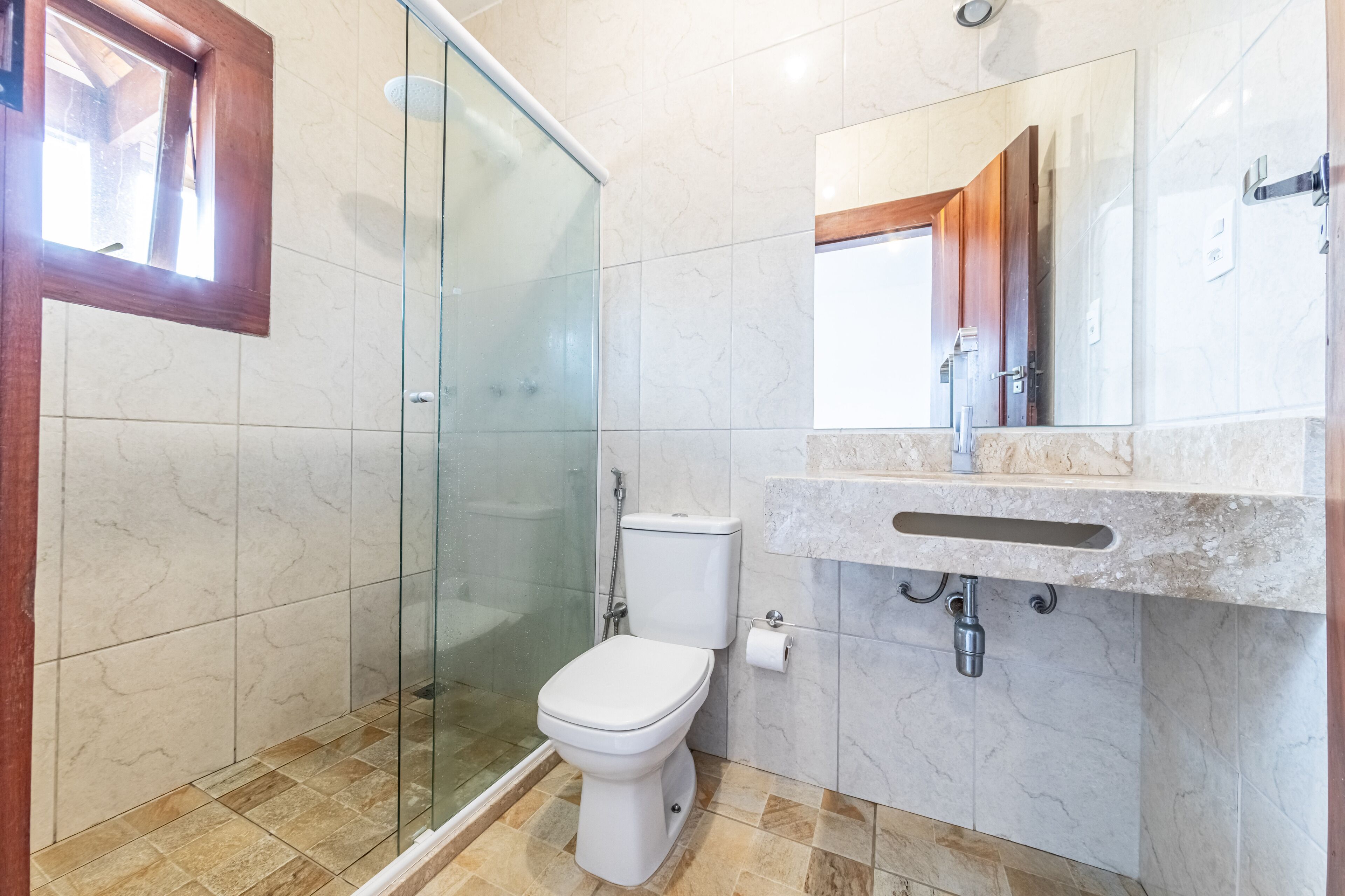 A bathroom with a glass shower enclosure, a toilet, a sink with a marble countertop, and a mirror above the sink.