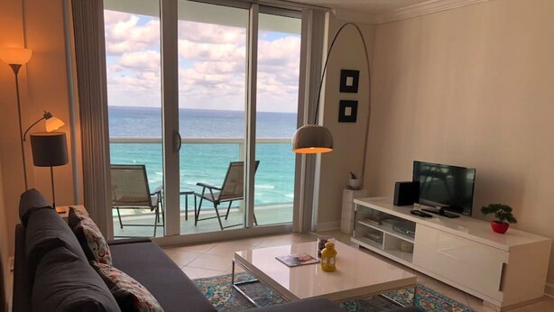 Una sala de estar moderna con un amplio ventanal corredero que da a un balcón con vistas al océano.