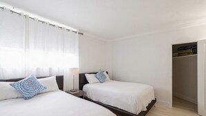 Habitación de hotel con dos camas, una mesita de noche, una lámpara y un armario.