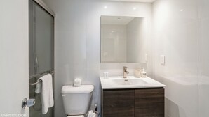 Un baño moderno con cabina de ducha de vidrio, inodoro blanco, tocador con espejo y mueble de madera oscura.