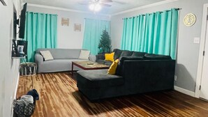 Un salon avec un canapé gris, un canapé noir, une table basse et un ventilateur de plafond.
