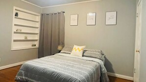 Une chambre à coucher avec un lit, une fenêtre avec des stores, une étagère fixée au mur et trois tableaux encadrés avec du texte.