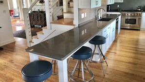 A modern kitchen with a central island, stainless steel appliances, and a staircase leading to another level. - Romantic Vineyard Retreat (Little Compton)
