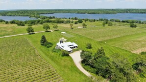 An aerial view of a property with a large house surrounded by lush green fields and a lake in the background. - Romantic Vineyard Retreat (Little Compton)