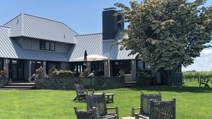 A large house with a stone wall and a patio with wooden chairs and tables. - Romantic Vineyard Retreat (Little Compton)