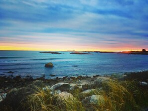 A coastal landscape with rocky shores, calm sea, and distant landforms under a clear sky. - Romantic Vineyard Retreat (Little Compton)