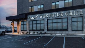 Un bâtiment dont la façade porte l’enseigne « WESTSIDE GRILL », caractérisé par un style architectural moderne, de grandes fenêtres et un parking situé devant.