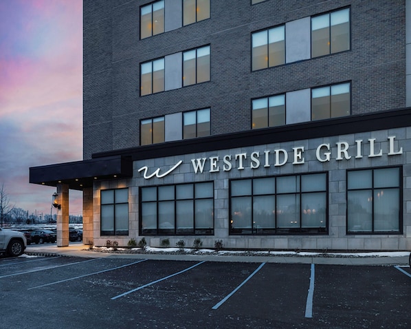 A building with the sign "WESTSIDE GRILL" on the facade, featuring a modern architectural style with large windows and a parking lot in front.
